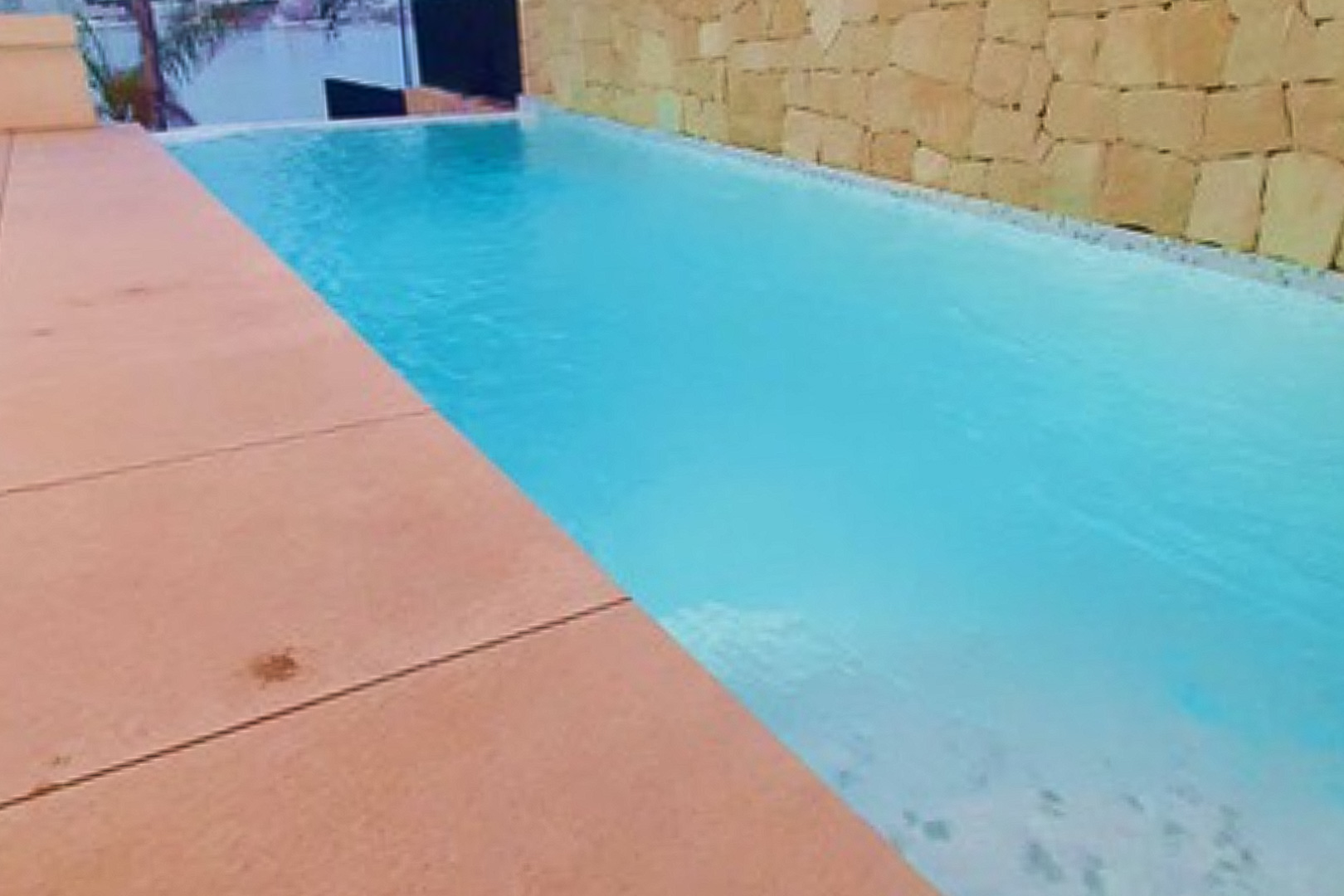 Privater Infinity-Pool mit Meerblick, eingefasst von einer Terrasse in Terrakotta-Optik und einer dekorativen Natursteinwand.