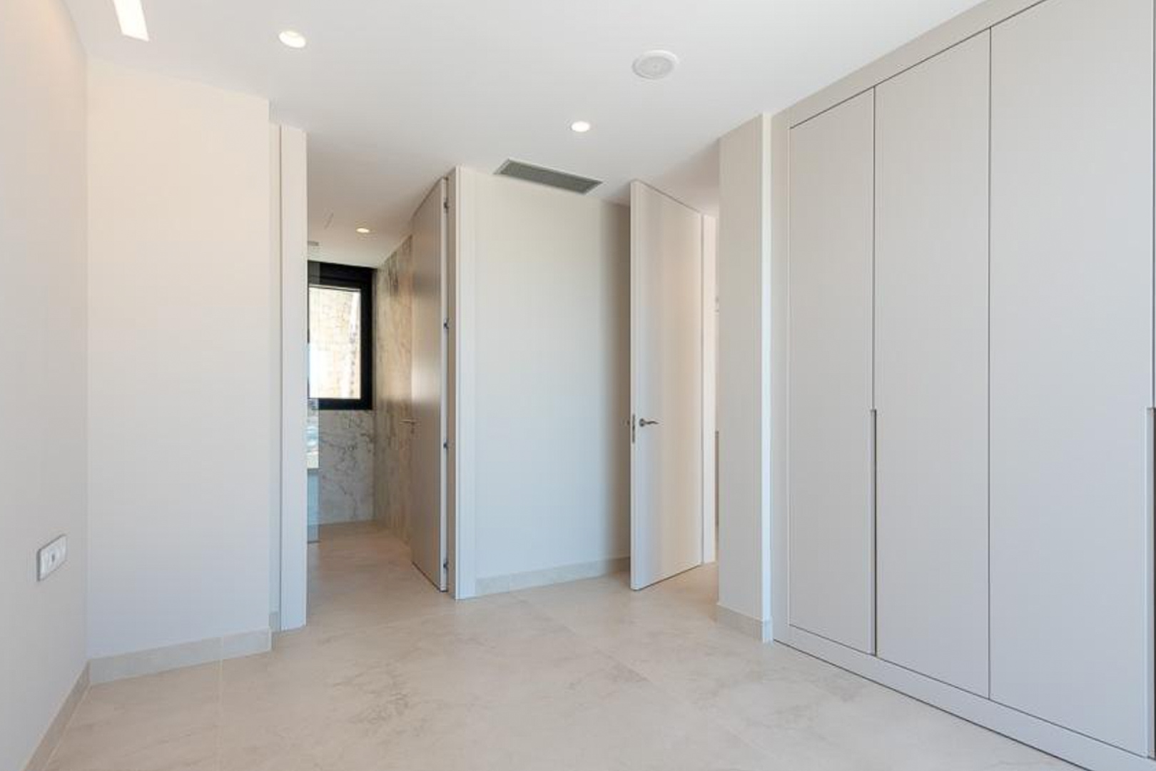 Schlafzimmer mit bodentiefen Einbauschränken, LED-Deckeneinbaustrahlern und Zugang zu einem En-Suite-Badezimmer mit Marmorverkleidung.