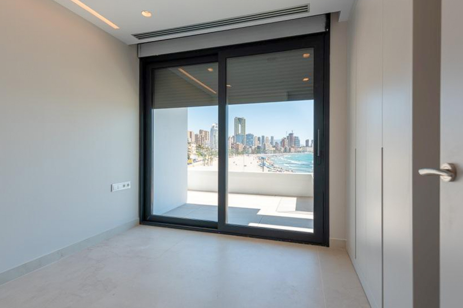 Schlafzimmer mit raumhohen Einbauschränken und direktem Zugang zur Terrasse mit Panoramablick auf den Strand und die Skyline von Benidorm.