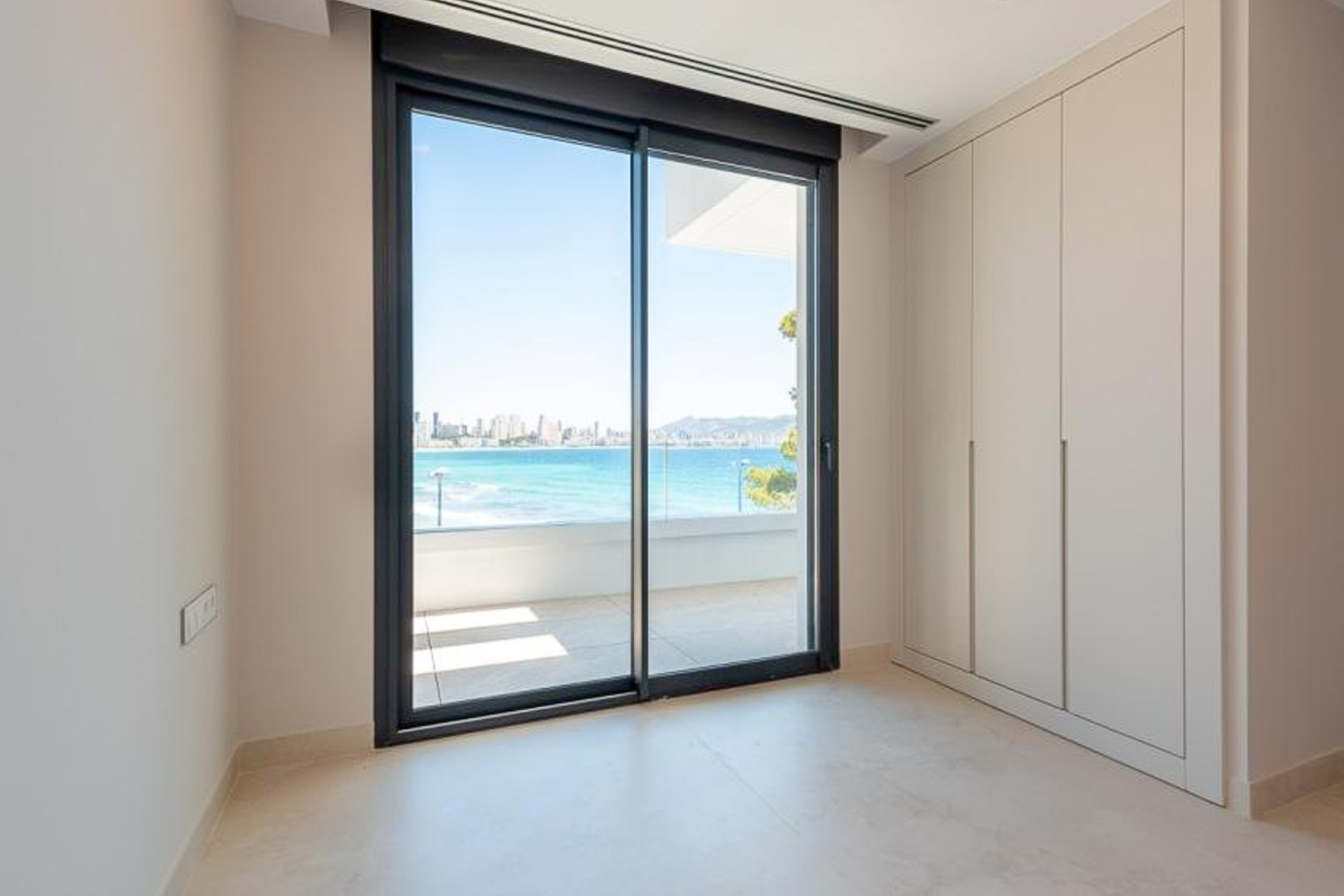 Schlafzimmer mit raumhohen Einbauschränken und großen Glasschiebetüren, die auf eine Terrasse mit Blick auf das Meer und Benidorm führen.
