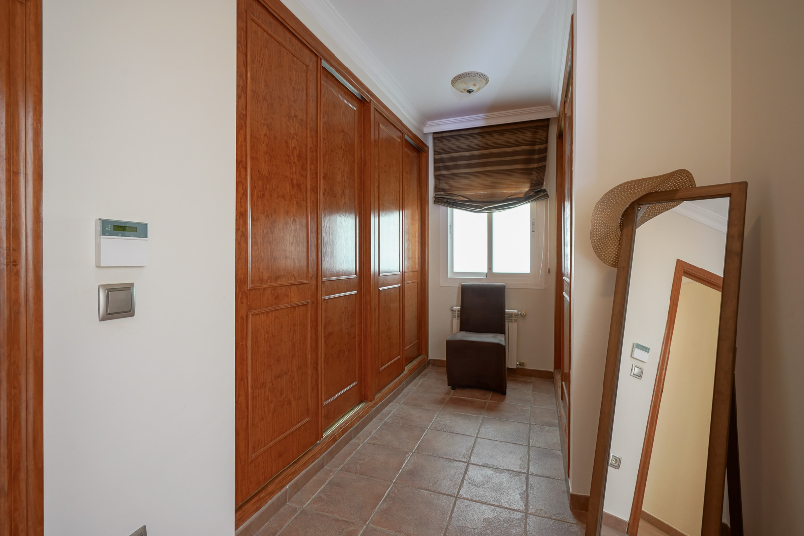 Ankleidebereich mit großen Einbauschränken aus Holz, Terrakotta-Fliesenboden und Fenster. Ausgestattet mit einem Ganzkörperspiegel und einem Beistellstuhl.