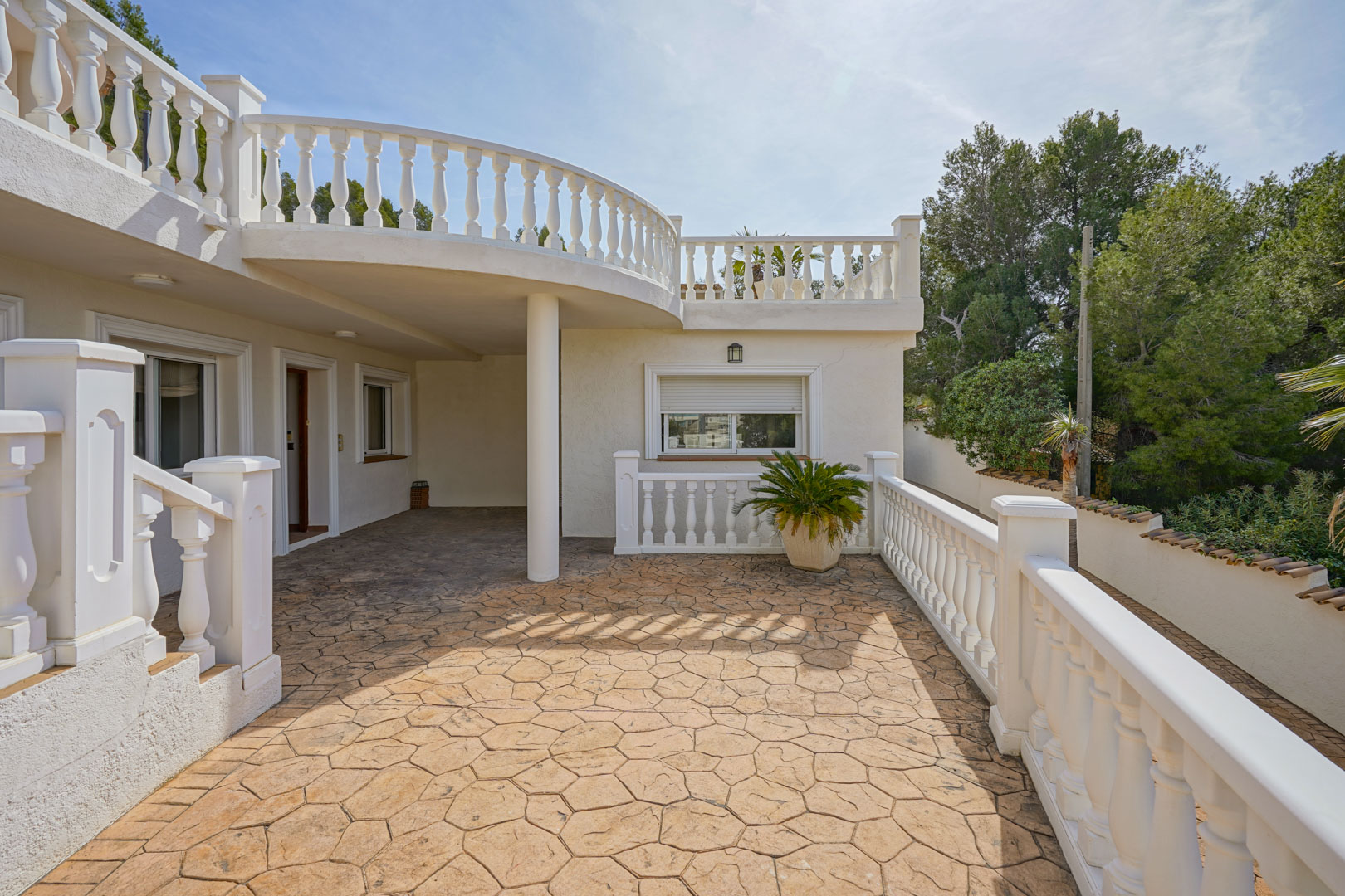 Außen-Terrasse mit geprägtem Betonboden und klassischen weißen Balustraden, gelegen unter dem geschwungenen Balkon der oberen Etage.
