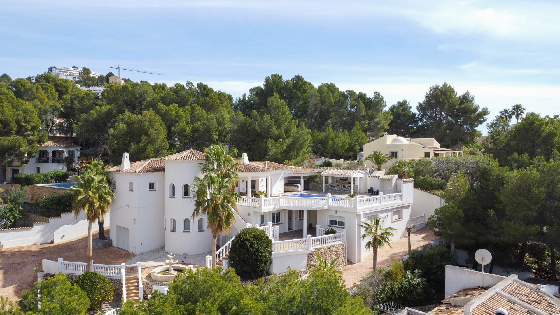 Außenansicht der mediterranen Villa mit weißer Fassade, Rundturm und weitläufigen Terrassen mit Balustraden, eingebettet in einen Pinienwald.