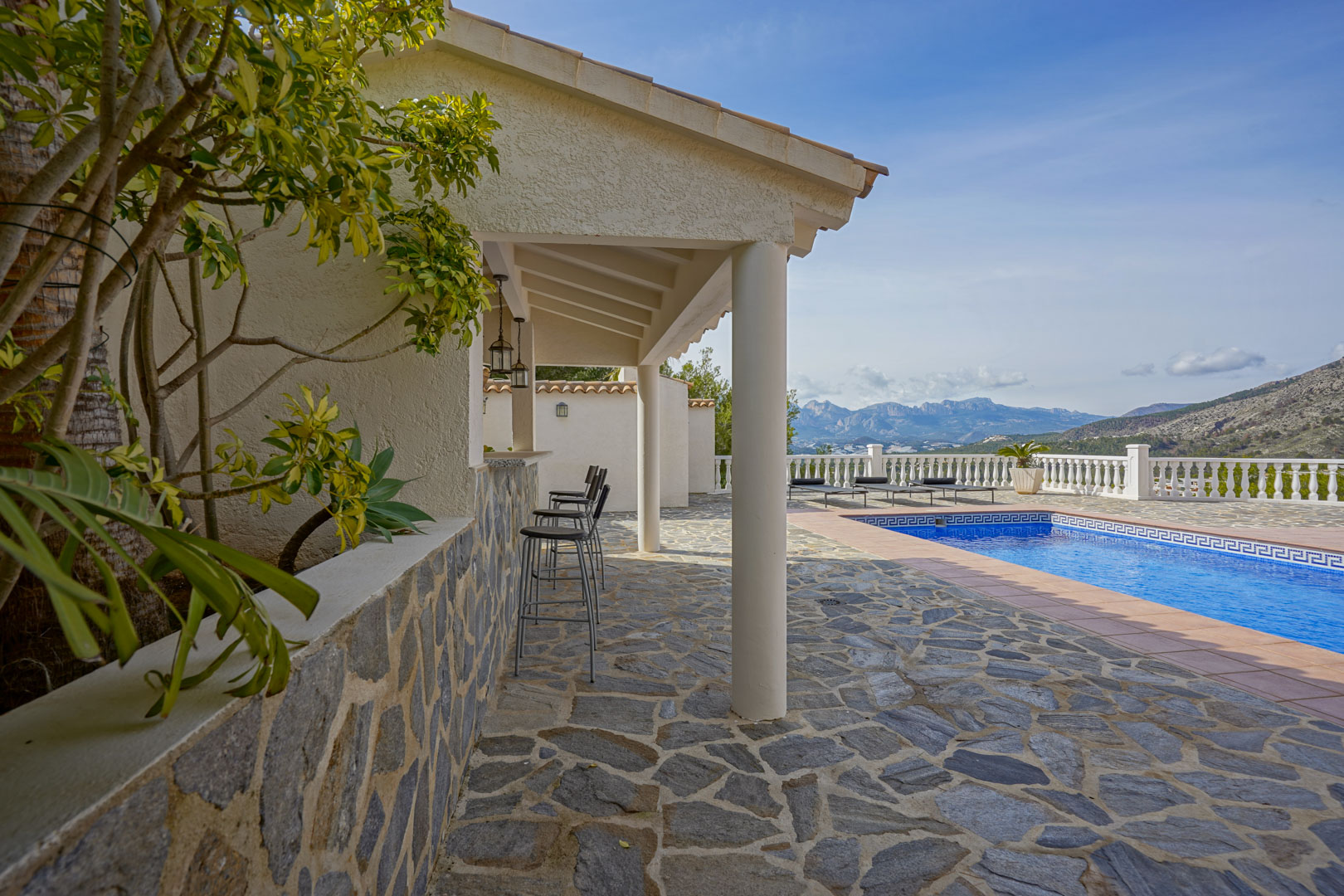 Außenbereich mit Natursteinboden, überdachter Sommerküche mit Bar und privatem Pool vor der Kulisse des majestätischen Bergpanoramas.