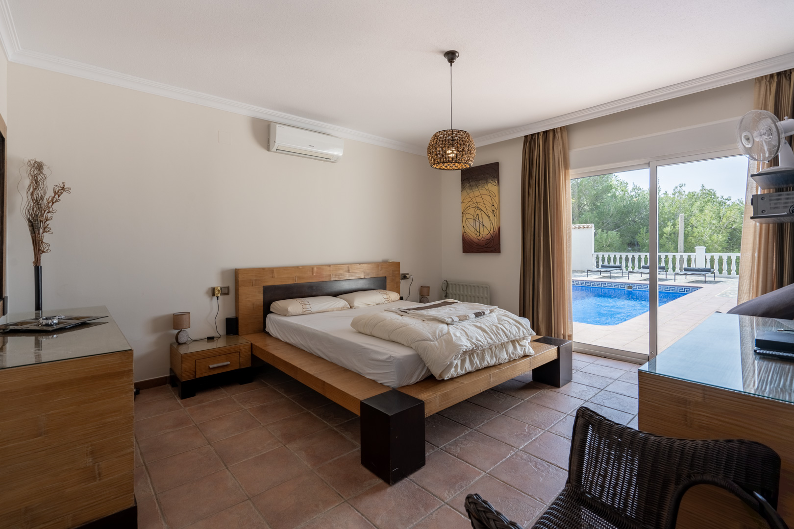 Hauptschlafzimmer mit Terrakottaboden, Klimaanlage und direktem Zugang zur Poolterrasse durch große Glasschiebetüren.