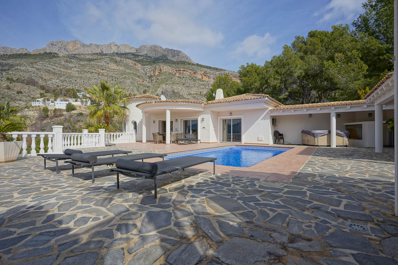 Hauptterrasse mit Pool und Natursteinpflasterung, die einen Panoramablick auf die Sierra de Bernia und die klassische weiße Architektur der Villa bietet.