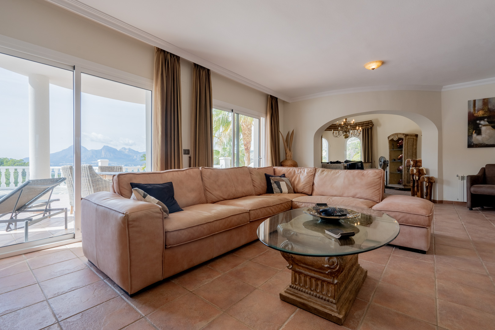 Helles Wohnzimmer mit Terrakottaboden, großzügigem Ledersofa und Glasschiebetüren, die einen weiten Blick auf die Berge und direkten Zugang zur Terrasse bieten.