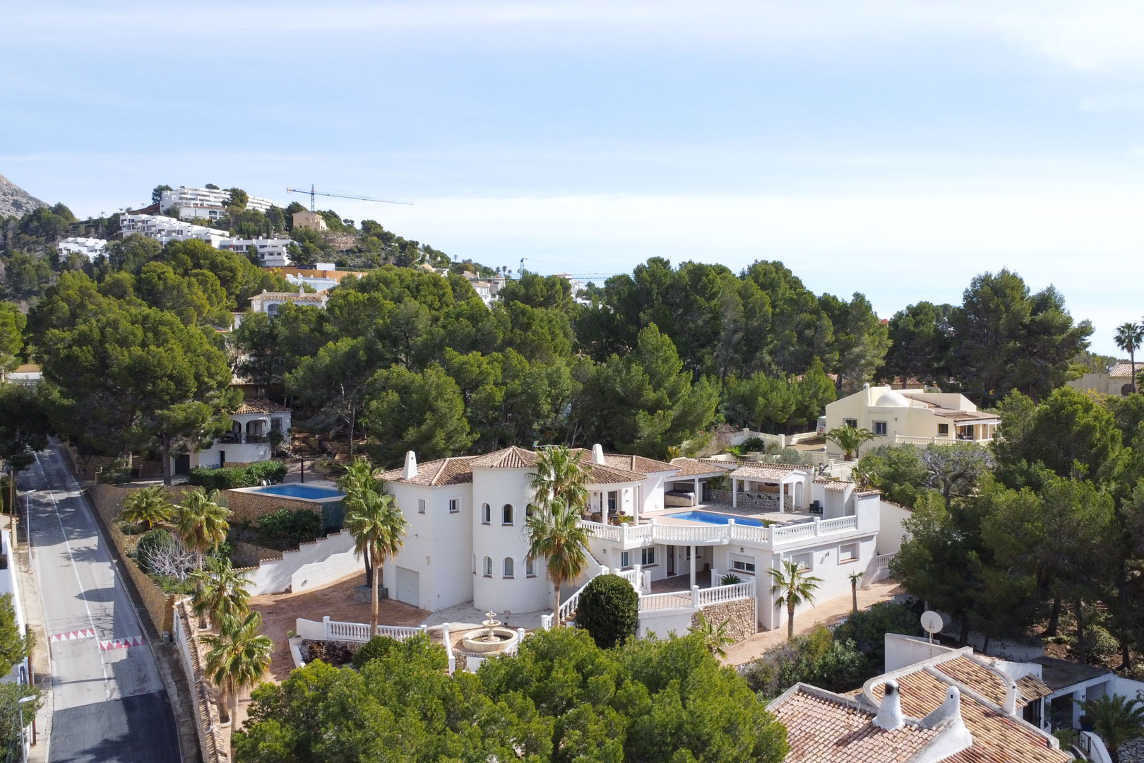 Luftaufnahme der mediterranen Villa mit weißer Fassade, Rundturm und Poolterrasse, eingebettet in eine grüne Pinienlandschaft in Altea.