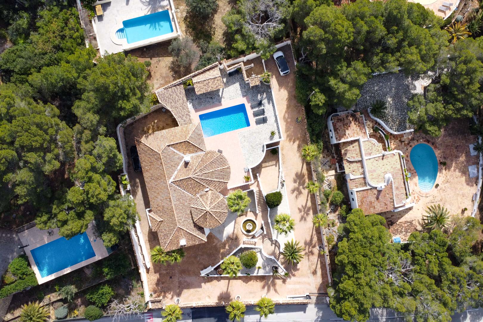 Luftaufnahme der Villa mit ihren Terrakotta-Ziegeldächern, dem rechteckigen Pool und den weitläufigen Steinterrassen inmitten mediterraner Vegetation.