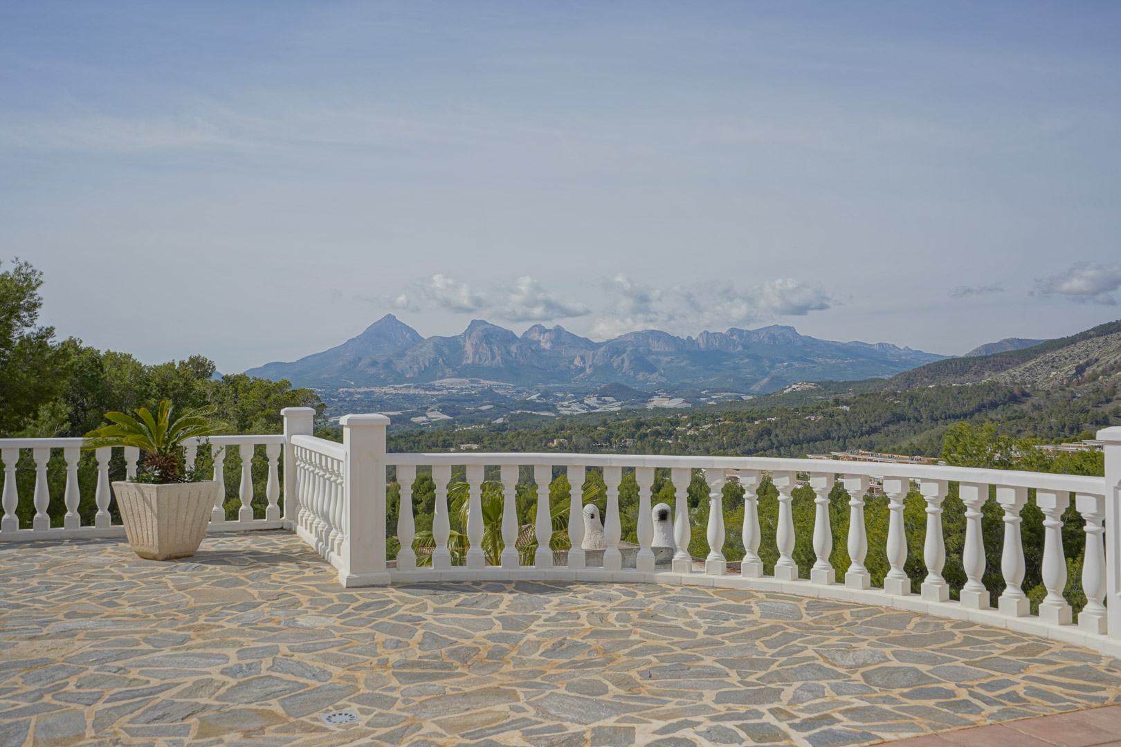 Natursteinterrasse mit weißer Balustrade und Panoramablick auf die Gebirgszüge Puig Campana und Sierra Aitana.