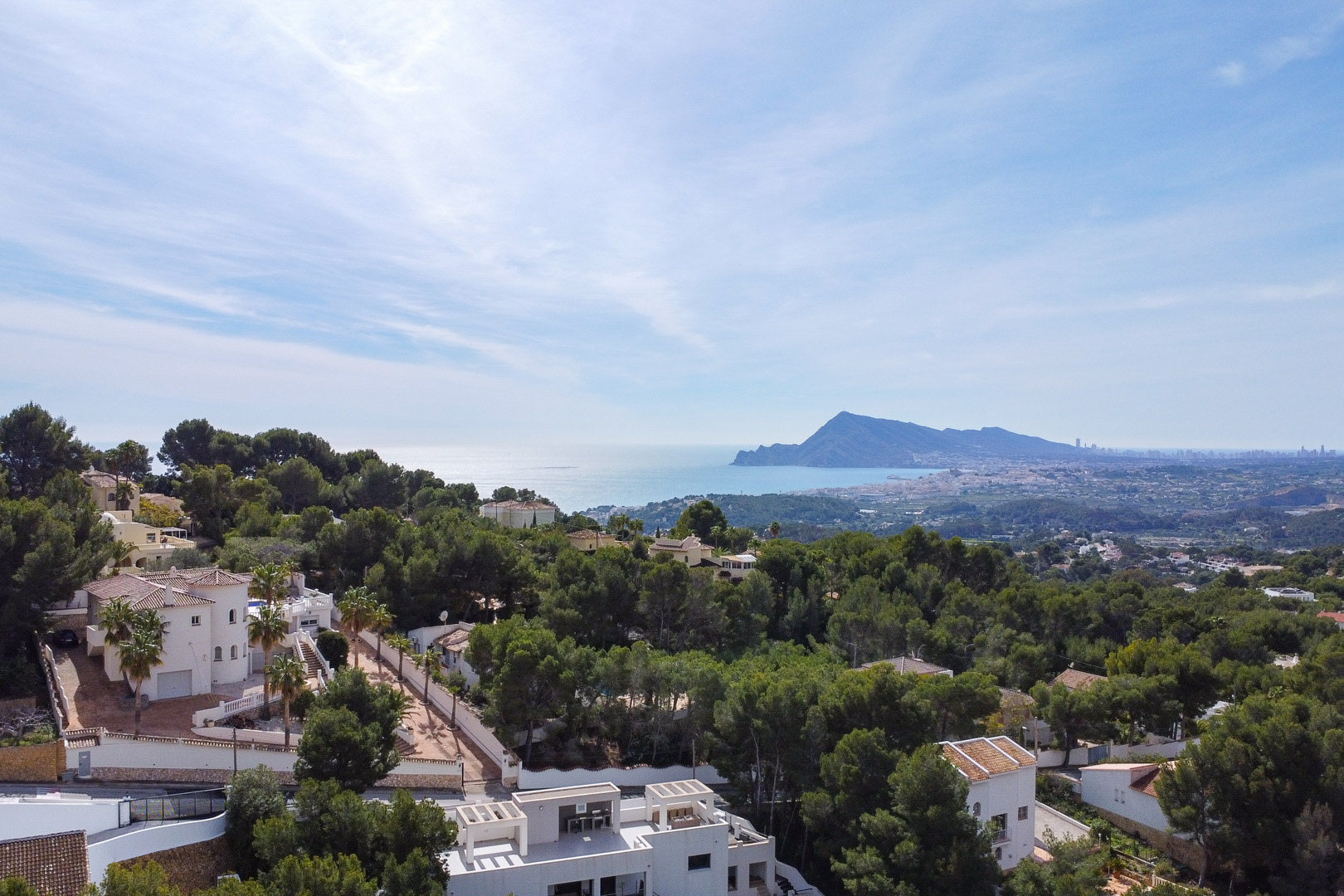 Panorama-Luftaufnahme der umliegenden Pinienwälder, weißen Villen und der Mittelmeerküste mit der Silhouette von Benidorm in der Ferne.