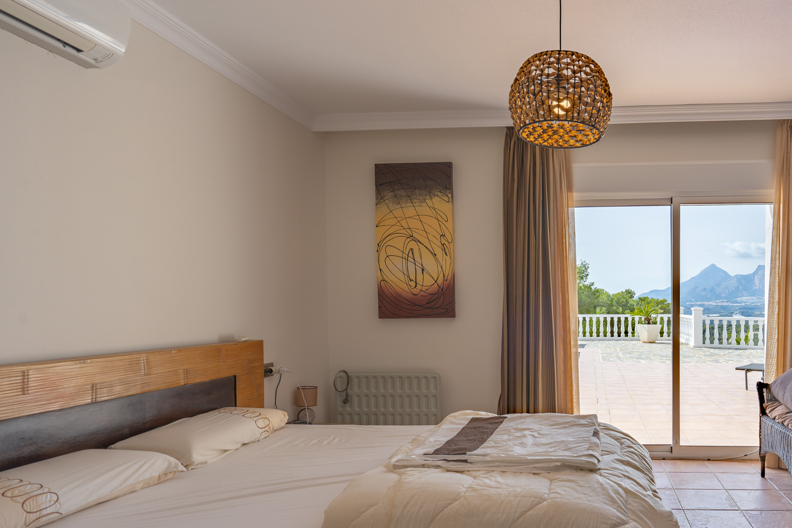 Schlafzimmer mit Holzkopfteil und Klimaanlage, inklusive direktem Terrassenzugang und weitem Blick auf die umliegende Berglandschaft.