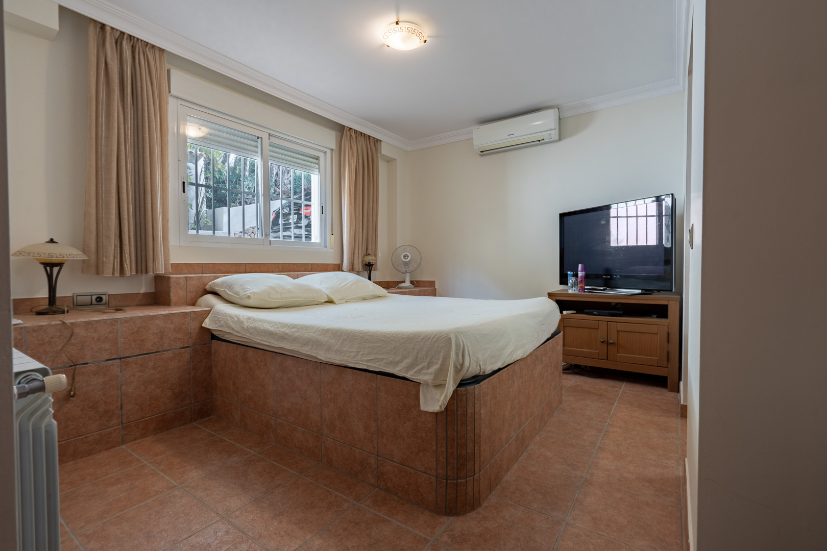 Schlafzimmer mit integriertem, gefliestem Bettgestell, Terrakotta-Fliesenboden, Klimaanlage und Heizkörper für optimalen Wohnkomfort.