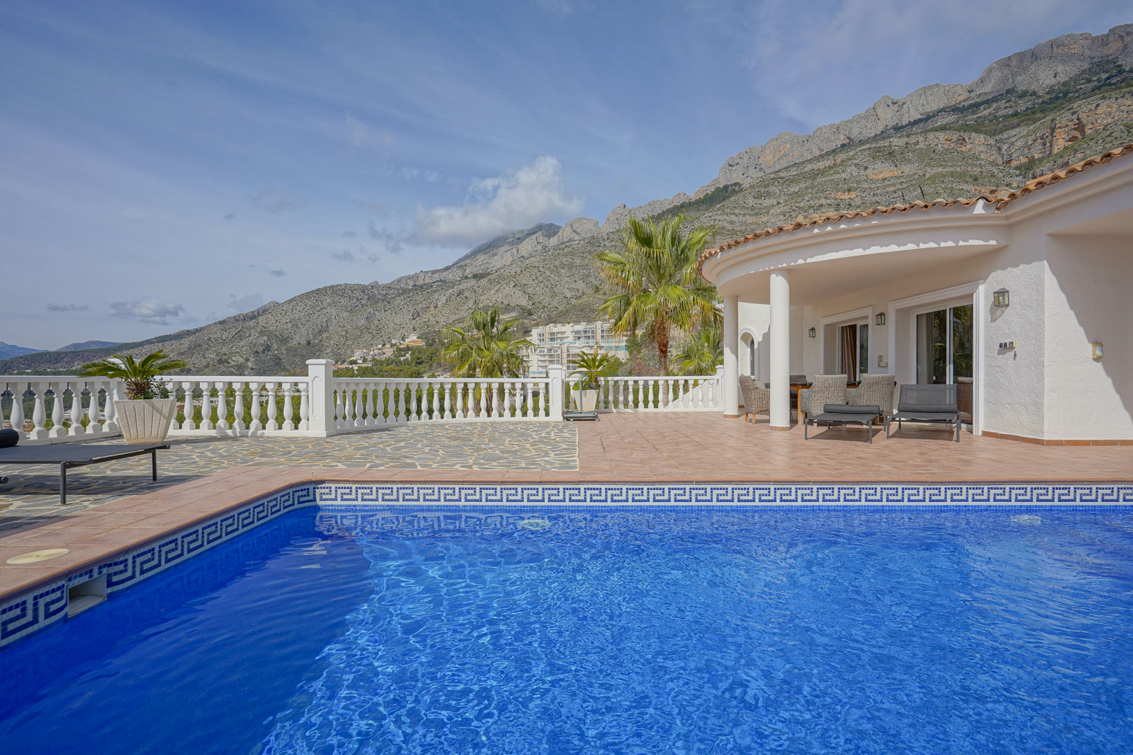 Terrasse mit blau gefliestem Pool und überdachter Veranda, die einen weiten Blick auf die Sierra de Bernia und die umliegende Bergwelt bietet.
