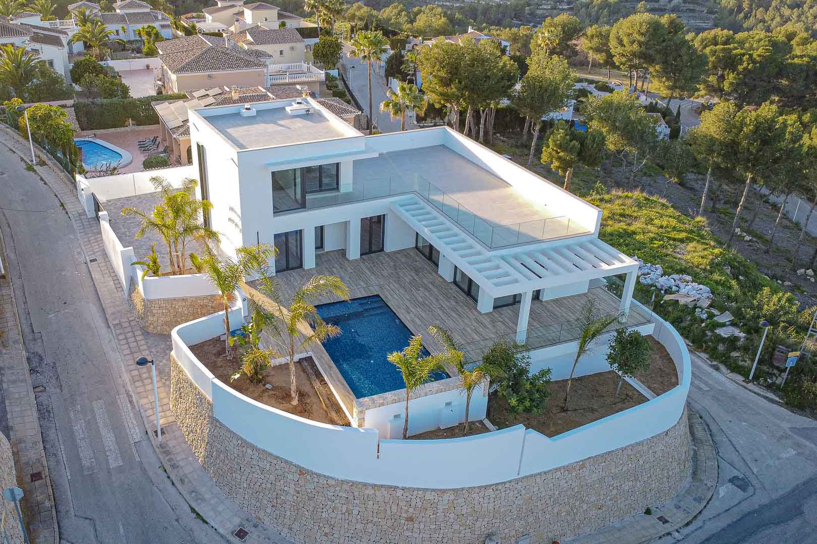 Luftaufnahme einer modernen Villa mit blauem Pool, Holzterrasse und mediterranem Garten in Benimeit, Moraira.