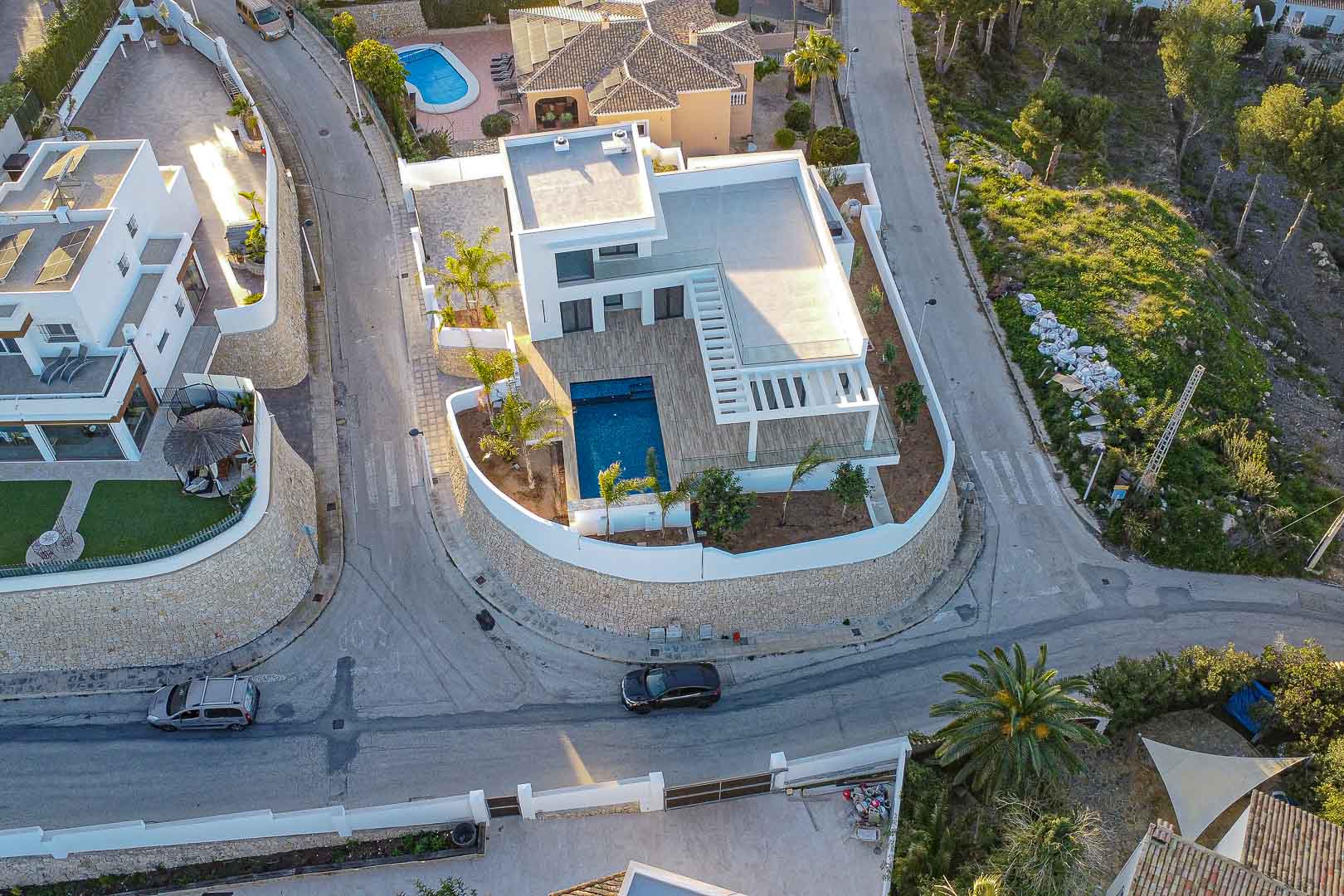 Luftaufnahme einer modernen Villa mit blauem Pool, Holzterrassen und mediterranem Garten in Benimeit, Moraira.