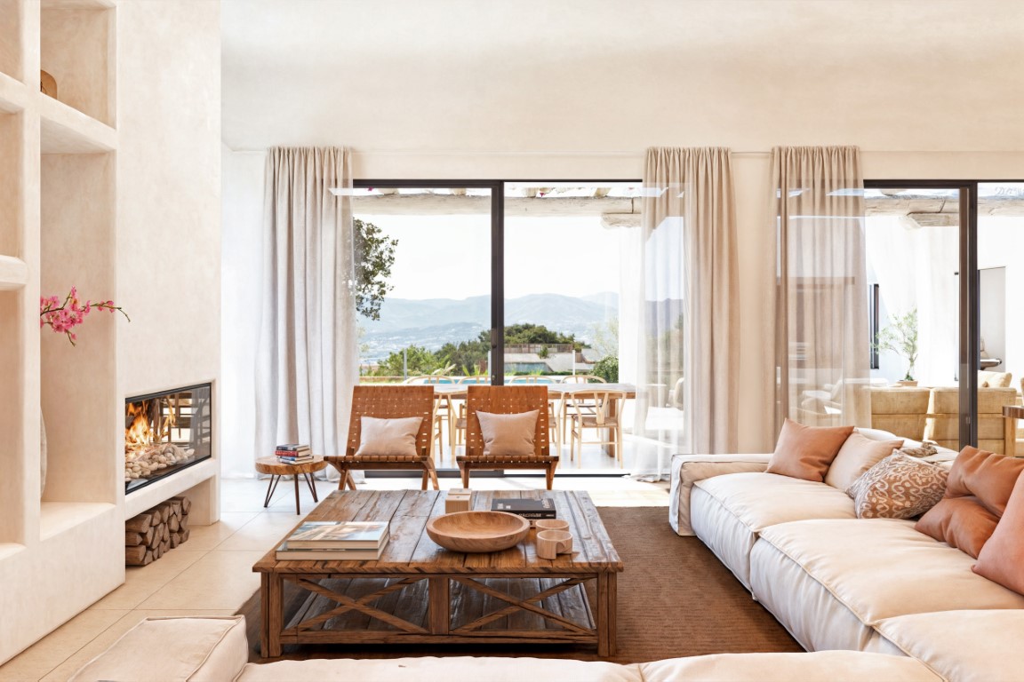 Helles Wohnzimmer mit integriertem Kamin, rustikalem Holzcouchtisch und großen Glasschiebetüren, die einen weiten Blick über das Tal und Zugang zur Terrasse bieten.
