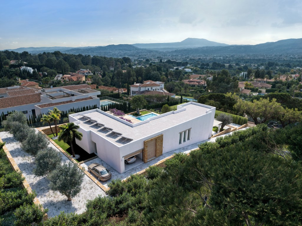 Luftaufnahme der modernen Villa in L-Form mit Solaranlage, integrierter Garage und mediterranem Garten mit Panoramablick auf das Tal.