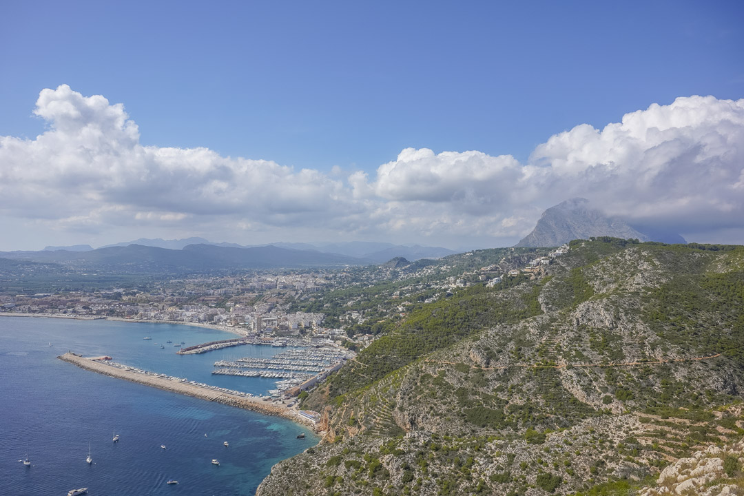 Luftaufnahme des Hafens von Jávea und der Küstenlinie, die das bergige Gelände und das markante Montgó-Massiv in der Ferne zeigt.