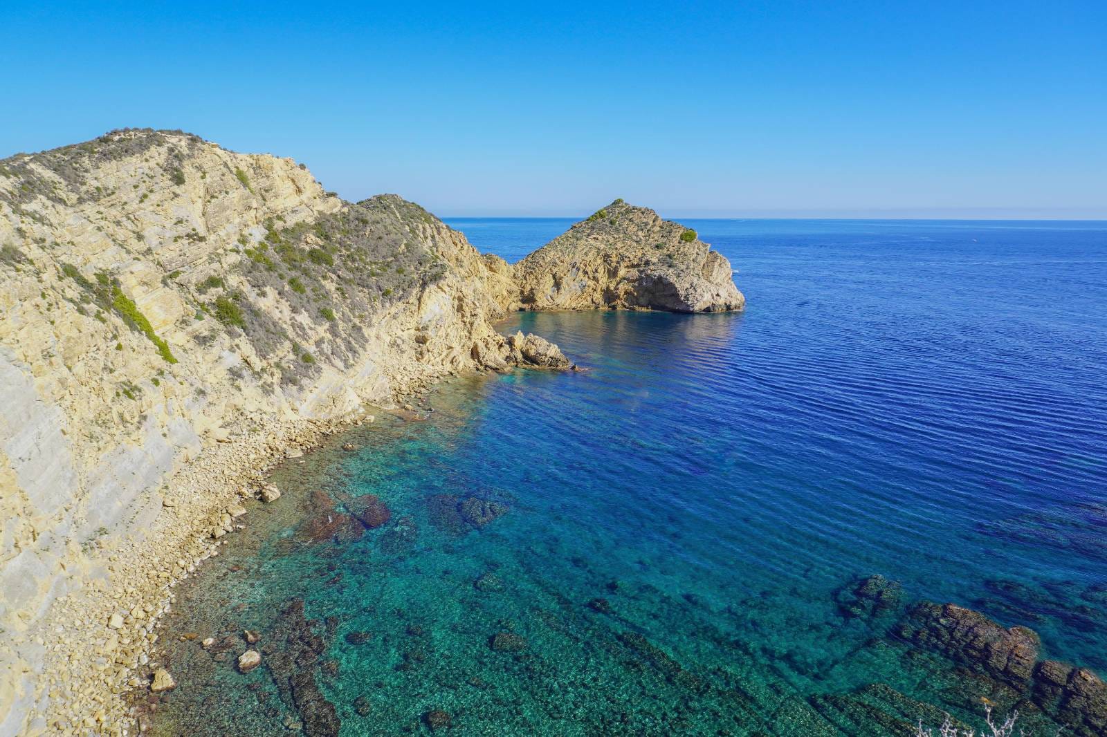 Panoramablick auf die Küste von Jávea mit markanten Kalksteinfelsen und kristallklarem, türkisblauem Mittelmeerwasser.