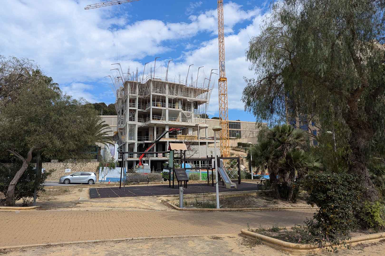 Aktueller Baufortschritt in Calpe mit der Stahlbetonstruktur und Baukränen direkt neben einem öffentlichen Spielplatz und Grünanlagen.