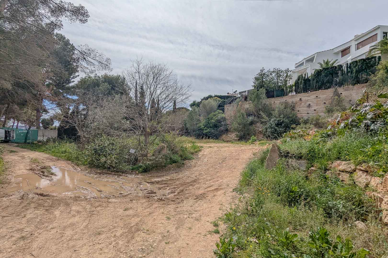 Erhöhtes Baugrundstück in La Corona mit natürlichem Gelände, umgeben von mediterraner Vegetation und angrenzenden Villen in Hanglage.