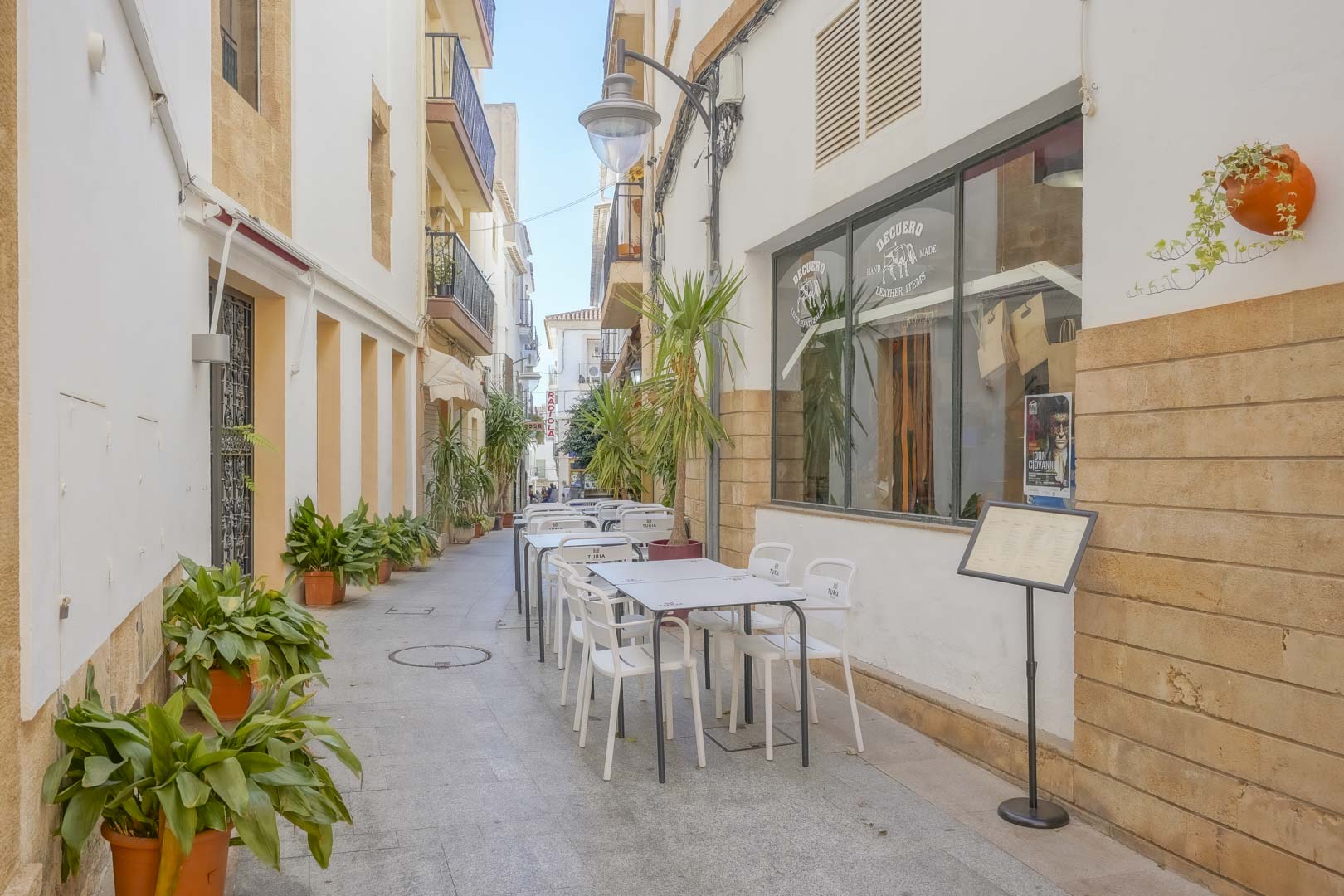 Fußgängerzone im Zentrum von Jávea mit weißen Fassaden, traditionellen Tosca-Stein-Akzenten und Außenterrassen mit mediterranen Kübelpflanzen.