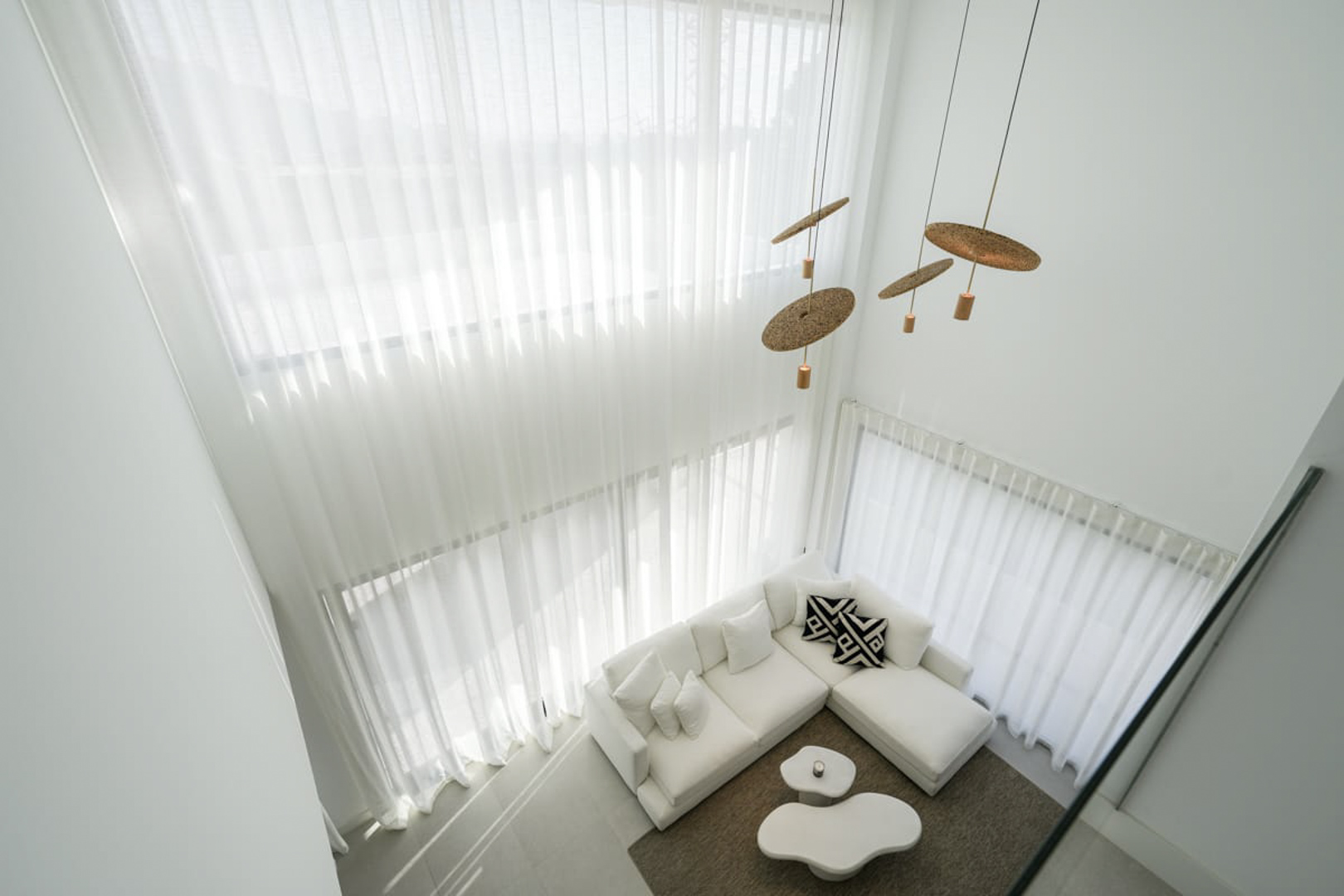 Erhöhte Ansicht des Wohnzimmers mit weißen Vorhängen, Ecksofa und Designer-Pendelleuchten.
