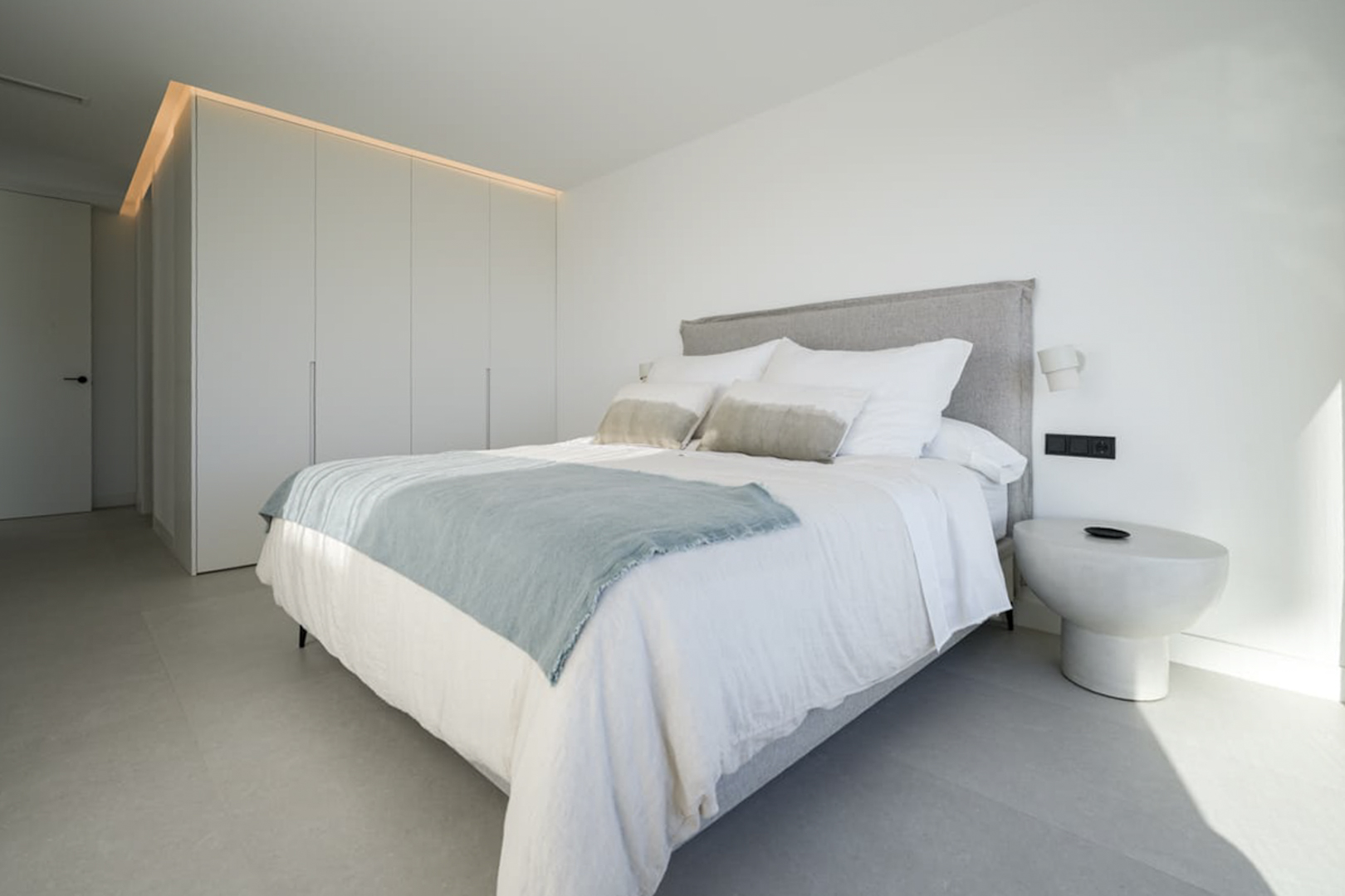 Helles Schlafzimmer mit Doppelbett, weißer Bettwäsche und Einbauschrank mit Oberbeleuchtung.