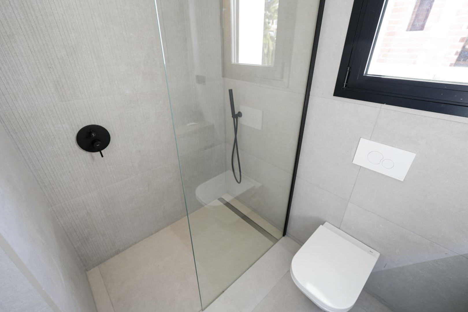 Modernes Badezimmerdetail mit Glasdusche, schwarzen Armaturen und grau strukturierter Fliesen.