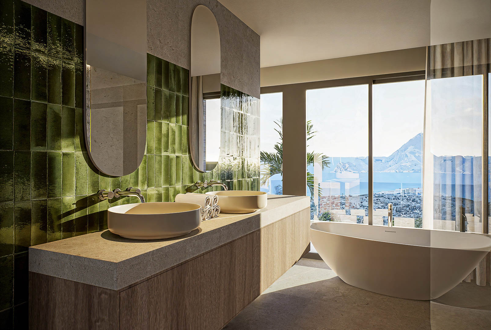 Hauptbadezimmer mit Doppelwaschbecken, grünen vertikalen Fliesen und einer freistehenden Badewanne mit direktem Blick auf das Meer und den Peñón de Ifach.
