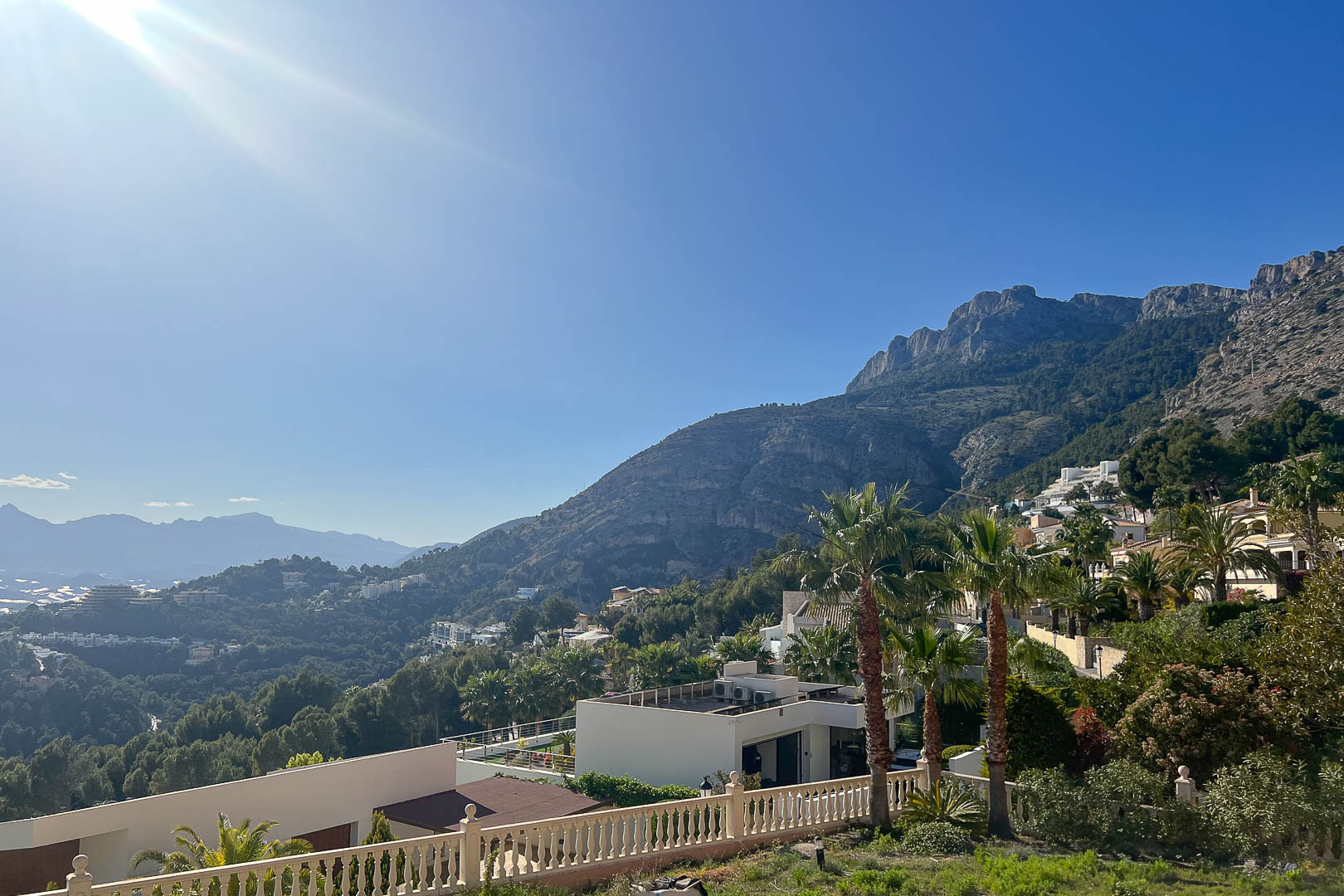 Panoramablick von Altea Hills auf das Sierra de Bernia Gebirge, weiße Villen am Hang und üppige mediterrane Vegetation unter strahlendem Himmel.