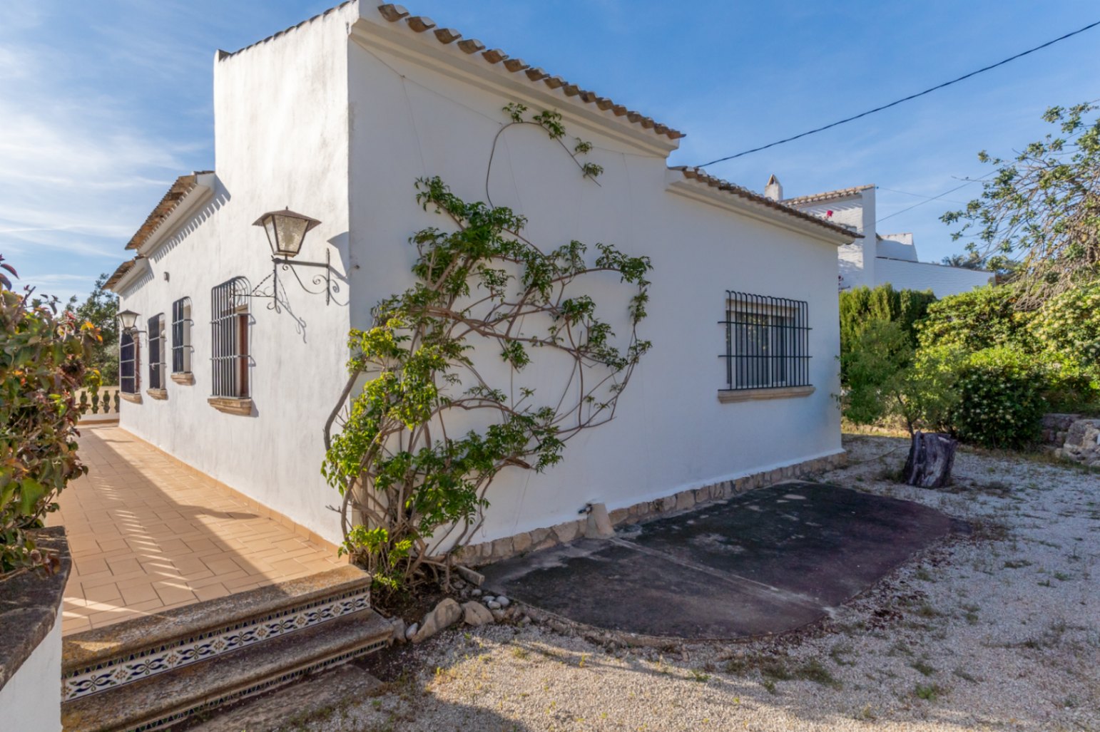 Außenansicht der Villa mit weißen Fassaden, schmiedeeisernen Fenstergittern und einer Terrasse mit dekorativen Keramikfliesen an den Treppenstufen.