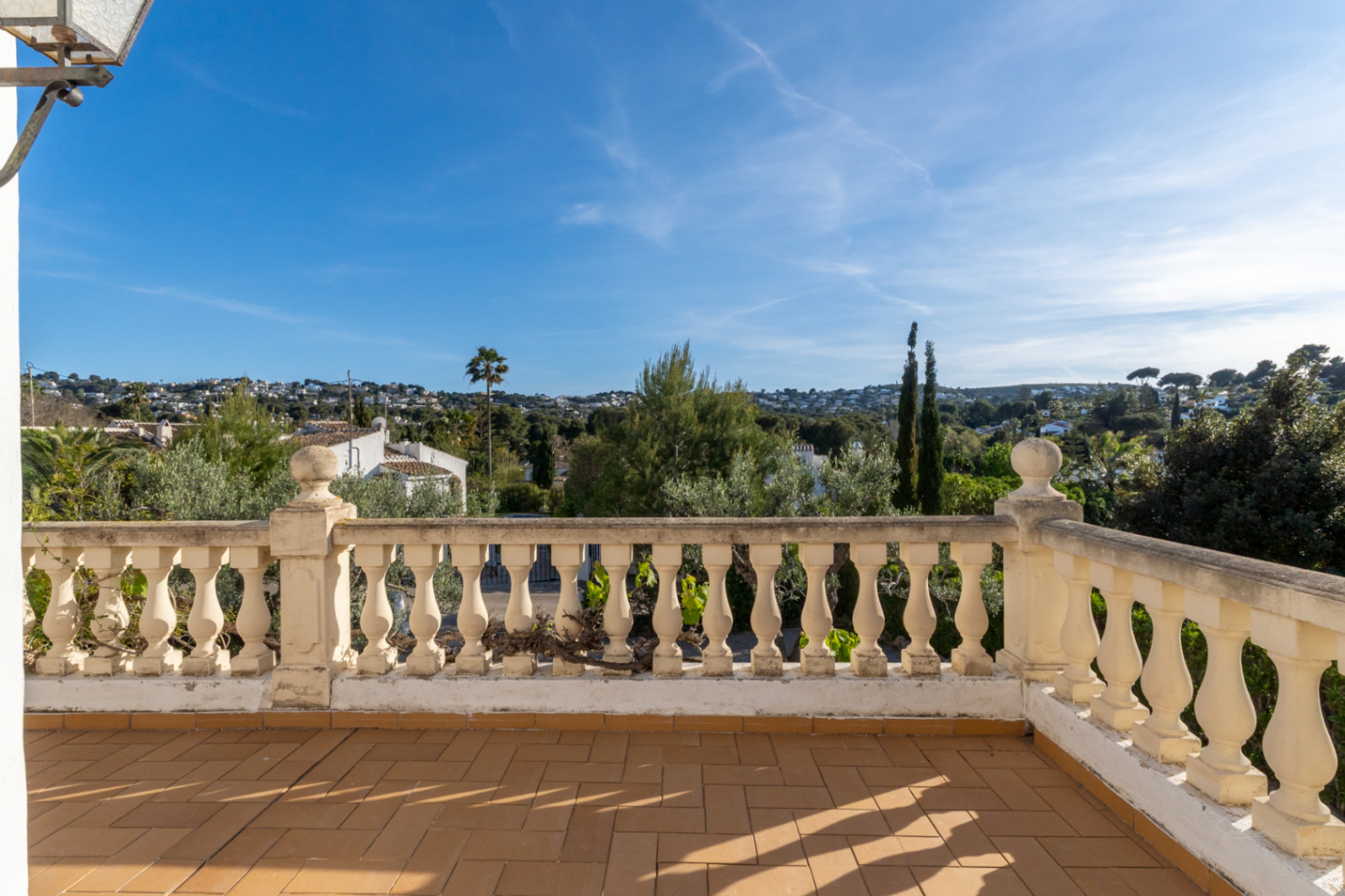 Erhöhte Terrasse mit traditionellen Terrakotta-Fliesen und klassischer Balustrade, mit weitem Blick über die grüne Wohngegend von Cap Martí in Jávea.