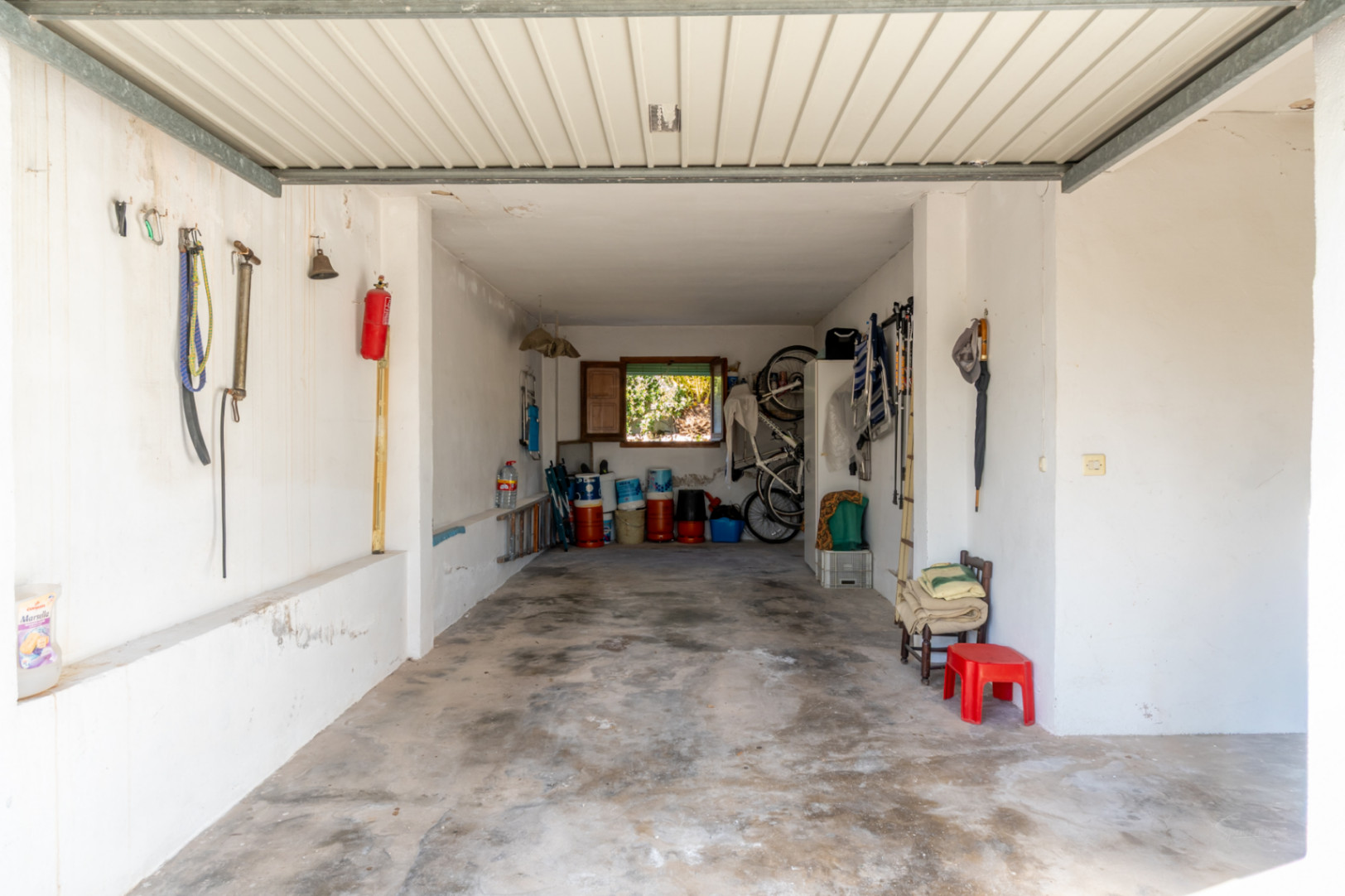 Funktionale Garage mit Betonboden und weißen Wänden, die viel Stauraum für Werkzeuge und Fahrräder bietet, mit Tageslicht durch ein rückwärtiges Fenster.