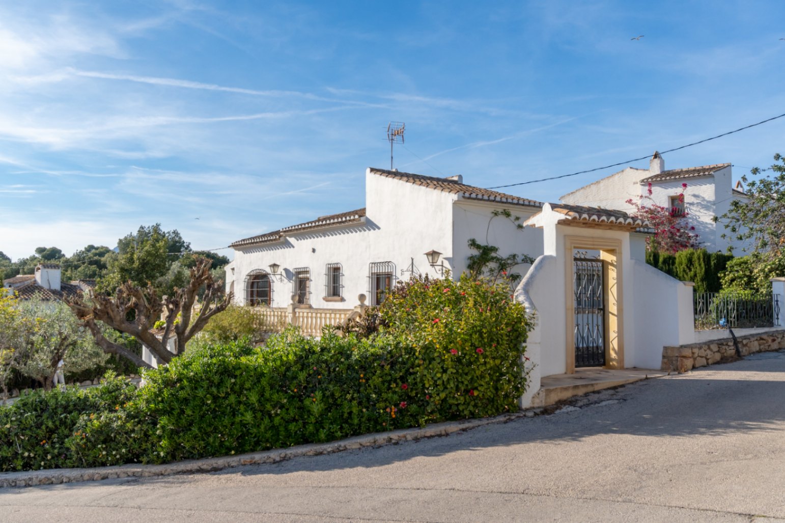 Mediterrane Außenansicht mit weiß getünchten Wänden, schmiedeeisernen Fenstergittern und einem steinernen Eingangstor mit traditionellem Ziegeldach.