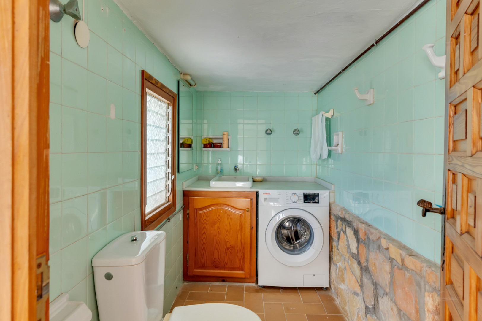 Waschküche und Gäste-WC mit mintgrünen Fliesen, Natursteinsockel, integrierter Waschmaschine und Holzunterschrank.
