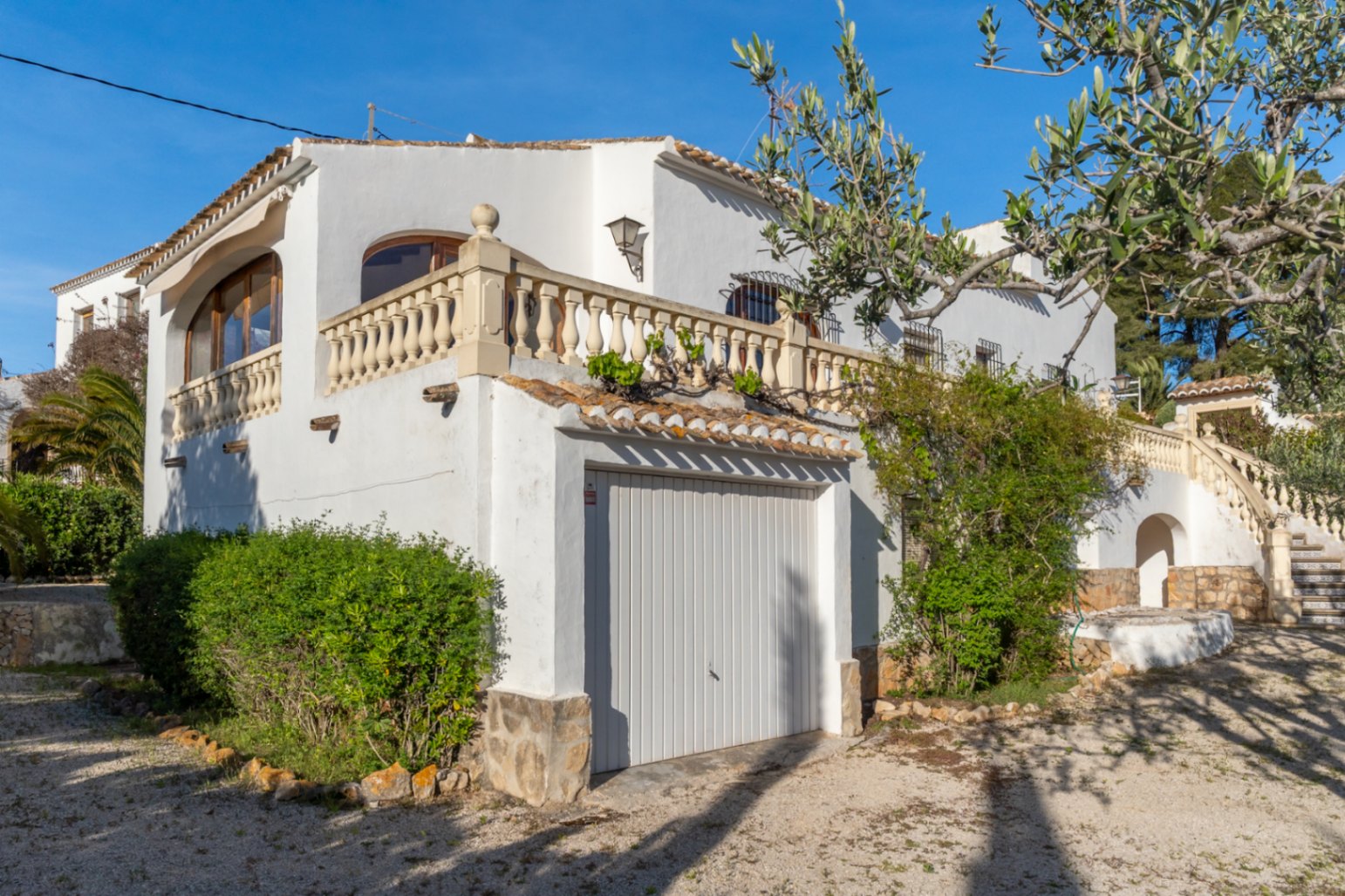 Weiße Fassade im mediterranen Stil mit integrierter Garage, traditioneller Steinbalustrade und einer mit Keramikfliesen verzierten Außentreppe.