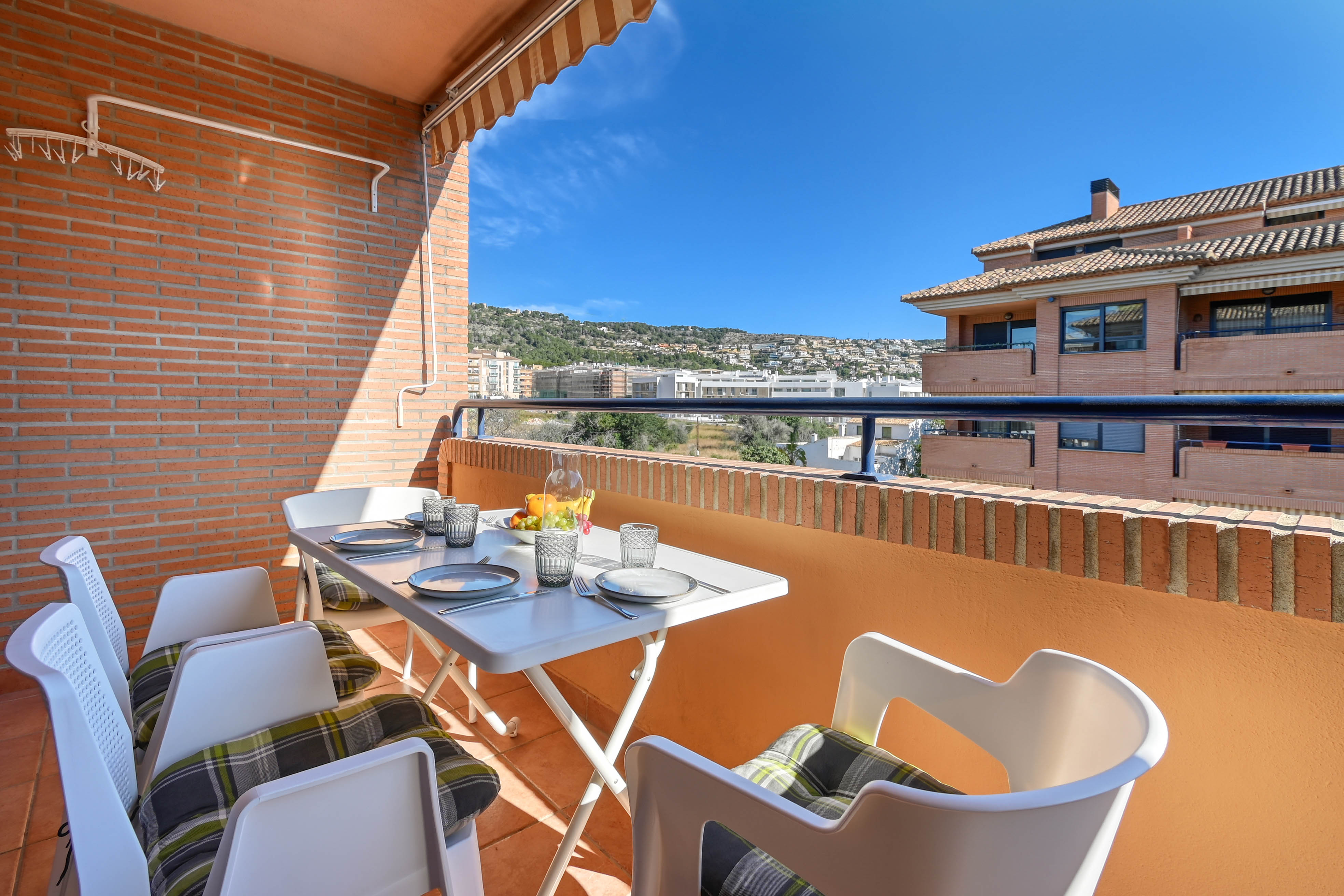 Private Terrasse mit Esstisch im Freien, gestreifter Markise und Backsteinwänden. Sie bietet einen freien Blick auf die Hügel und die Wohngegend von Jávea.