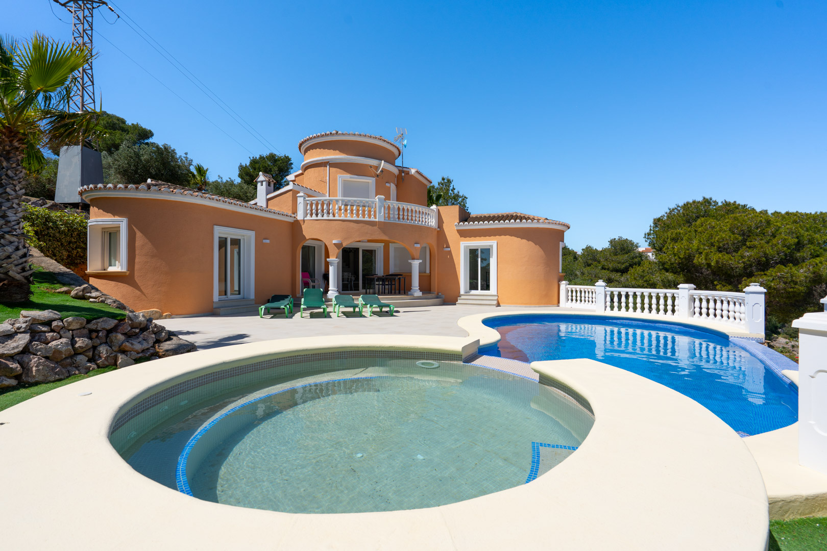 Außenansicht der Villa mit geschwungenem Pool, integriertem Rundbecken, großzügiger Terrasse und mediterraner Architektur in warmen Erdtönen.