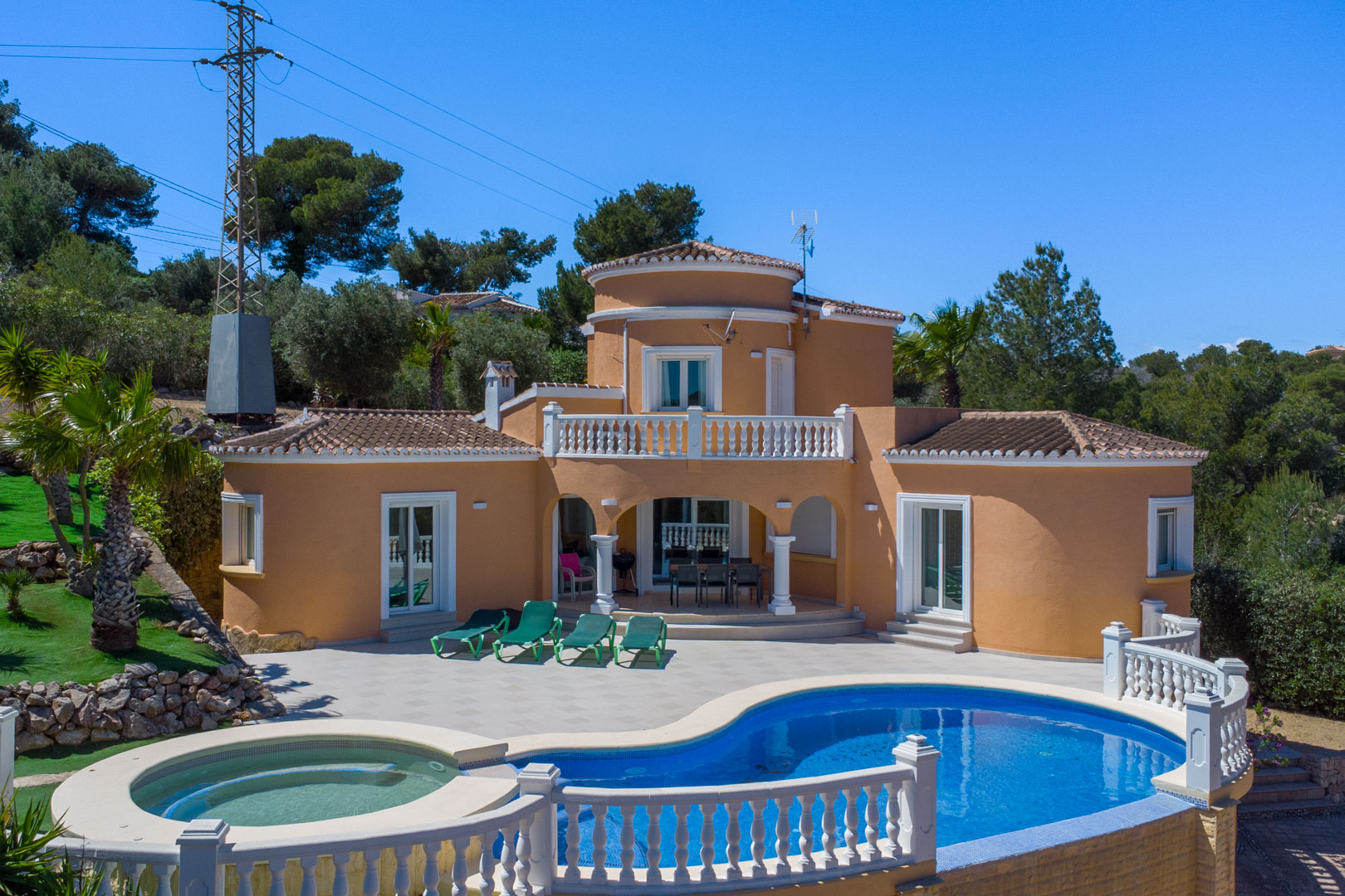 Außenansicht der Villa mit geschwungenem Pool, integriertem Whirlpool und großzügiger Terrasse. Die mediterrane Fassade wird durch weiße Balustraden und Säulen ergänzt.