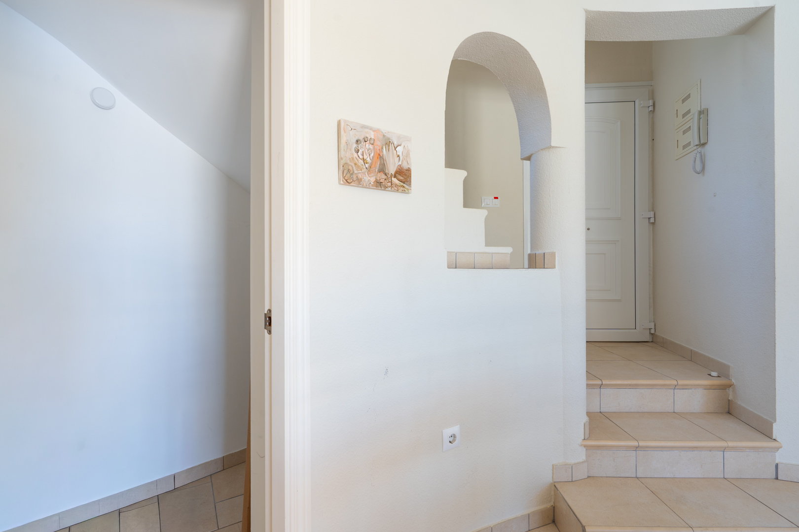 Eingangsbereich mit kurzer Innentreppe, neutralen Keramikfliesen und einer dekorativen Rundbogenöffnung in der Wand.
