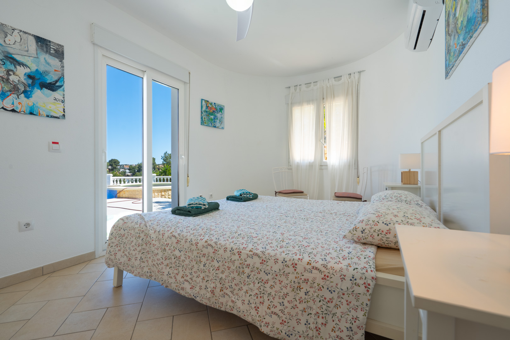 Helles Schlafzimmer mit direktem Zugang zur Terrasse und zum Pool, ausgestattet mit Klimaanlage, Fliesenboden und weißen PVC-Fenstern.