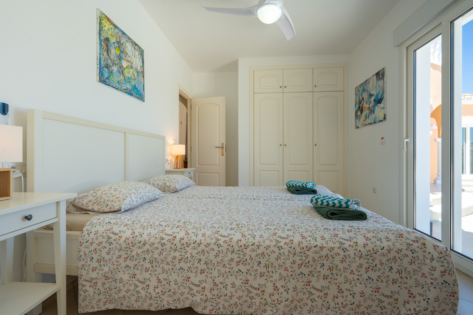 Helles Schlafzimmer mit Einbauschränken, Deckenventilator und direktem Zugang zur Terrasse durch doppelt verglaste PVC-Schiebetüren.