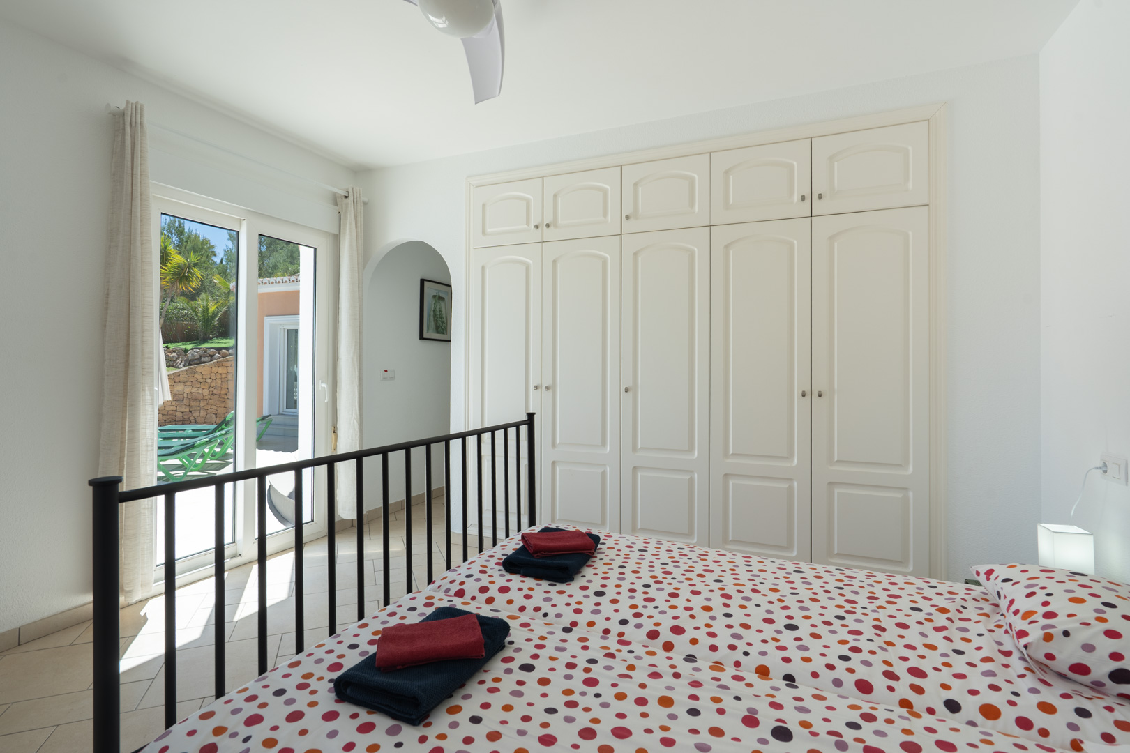 Helles Schlafzimmer mit weißen Einbauschränken, Deckenventilator und direktem Zugang zur Terrasse durch PVC-Schiebetüren.