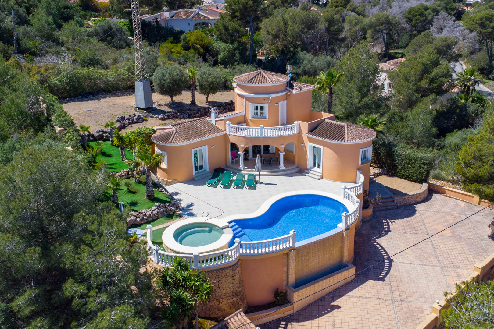 Luftaufnahme der mediterranen Villa mit nierenförmigem Pool, integriertem Jacuzzi, weitläufiger Fliesenterrasse und traditioneller Architektur.