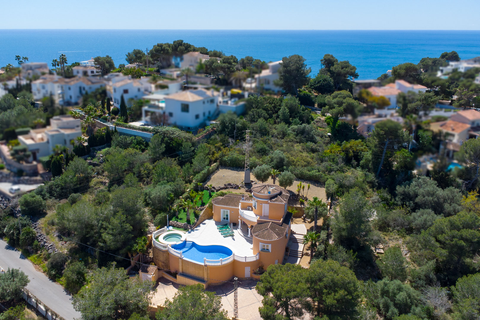 Luftaufnahme der Villa mit terrakottafarbener Fassade, nierenförmigem Pool mit weißen Balustraden und weitem Blick auf das Mittelmeer und die umliegende Vegetation.