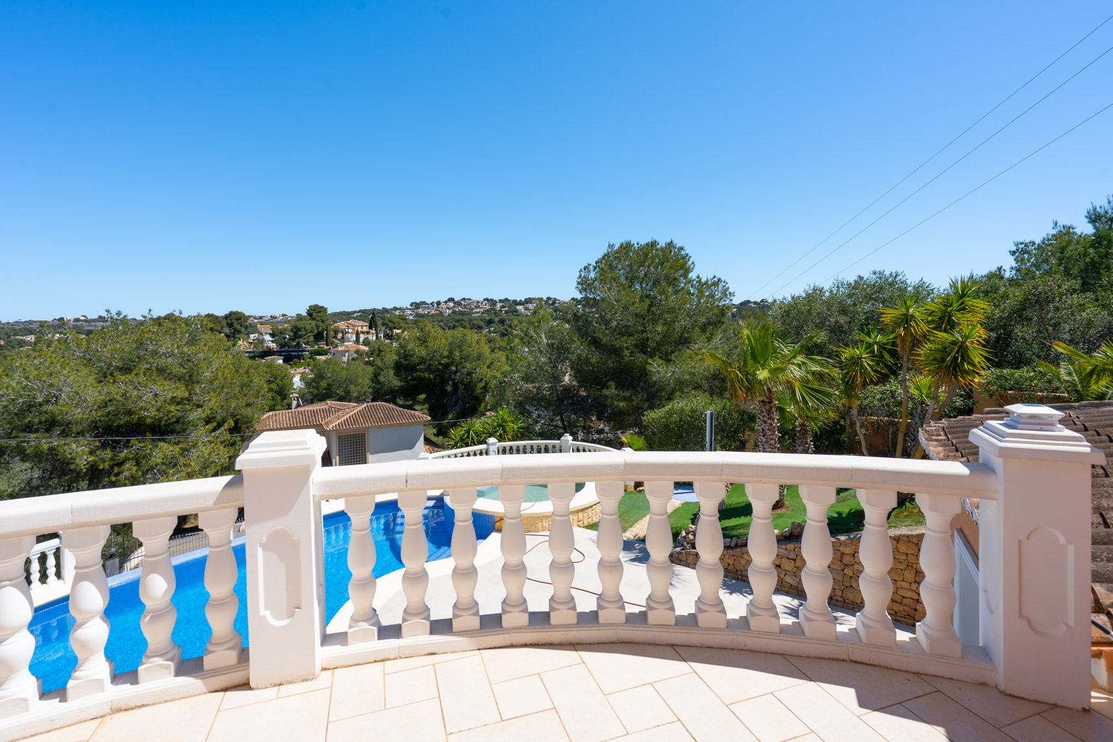 Obere Terrasse mit klassischer weißer Steinbalustrade und Blick auf den privaten Pool, den gepflegten Garten und die umliegenden Hügel von Jávea.