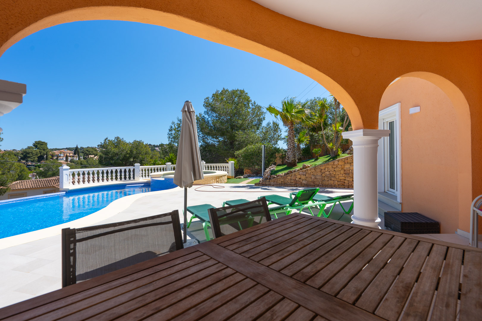 Überdachte Terrasse mit traditionellen Rundbögen, Blick auf den privaten Pool, Sonnenliegen und den mediterran angelegten Garten mit Natursteinmauern.