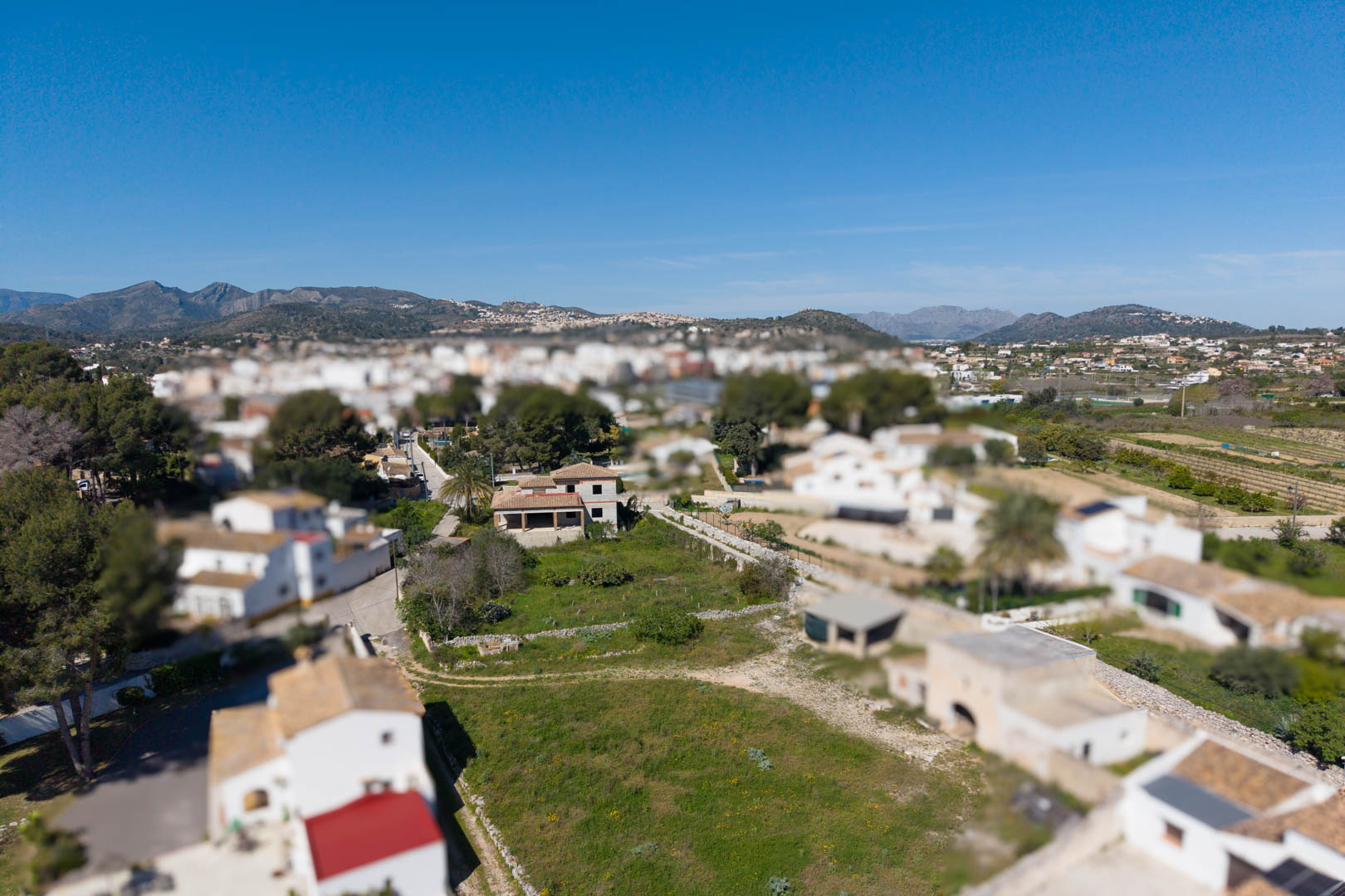 Luftaufnahme des 1800 m² großen Grundstücks mit dem Rohbau des Haupthauses und Nebengebäuden vor einer bergigen Kulisse.